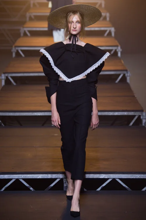 Simon Porte Jacquemus: người mẫu mặc áo crop top tay dài có yếm màu đen, quần tây ống cropped màu đen và đội mũ cói.