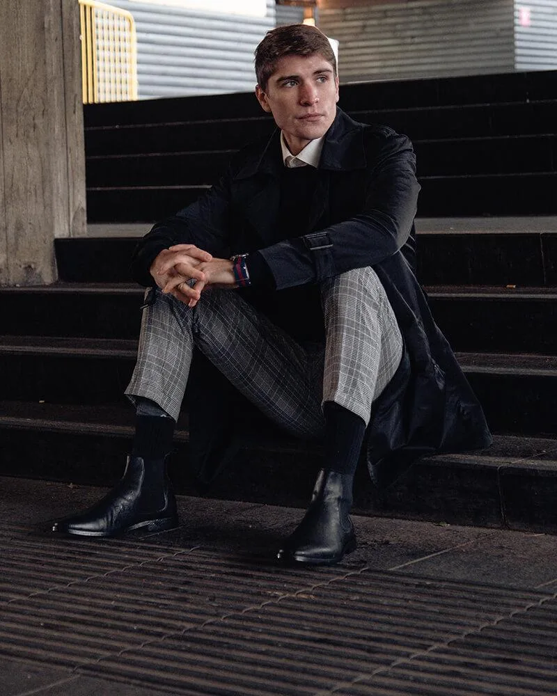 chàng trai mặc áo đen, quần tây xám và giày chelsea boots đen.
