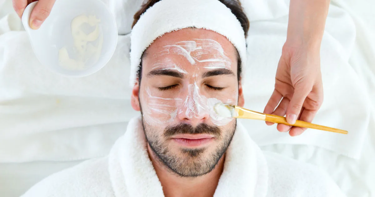 Portrait of man with clay facial mask in beauty spa.