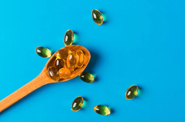 Omega 3 pills on the wooden spoon on the blue background with copy space