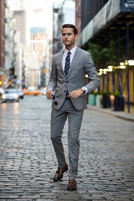 9 điều về suit nam cần lưu ý: người đàn ông mặc suit xám, tay cầm kính mát.